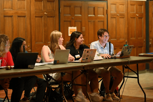 Five students sitting at a desk with laptops in front of them